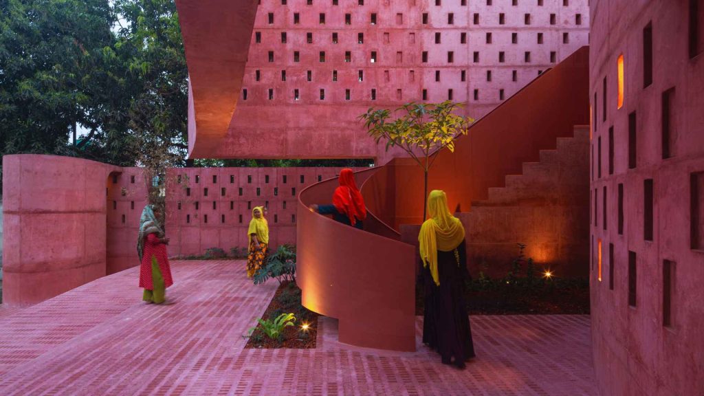 Women walking inside pink concrete mosque interior.