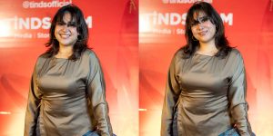 Amrin Tasnim Jaima at TINDS Social Dhaka smiling warmly in a bronze satin top against a vibrant red brand backdrop during a media event.